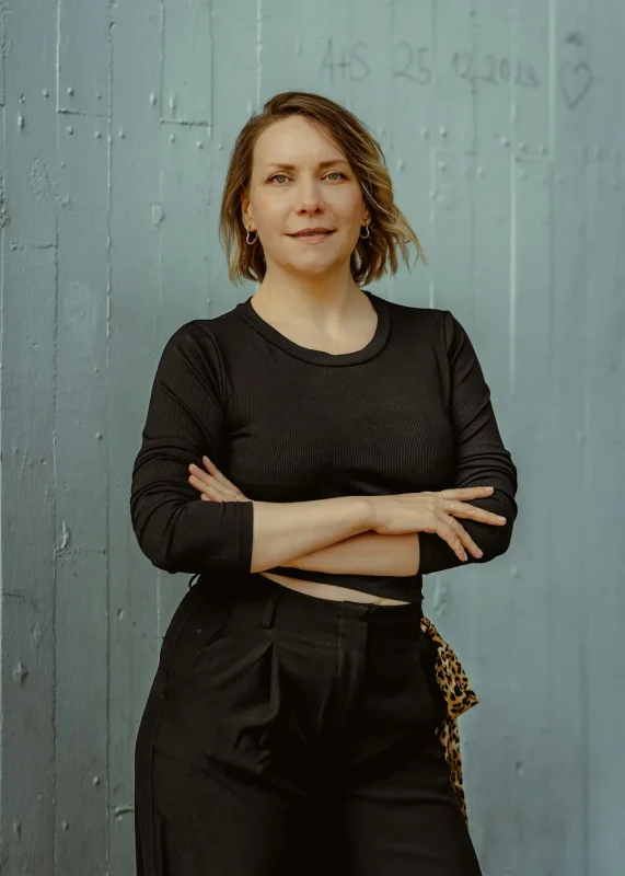 Lena Varga standing against a gray wall with her arms folded