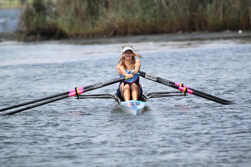 A woman rowing a single scull on calm water